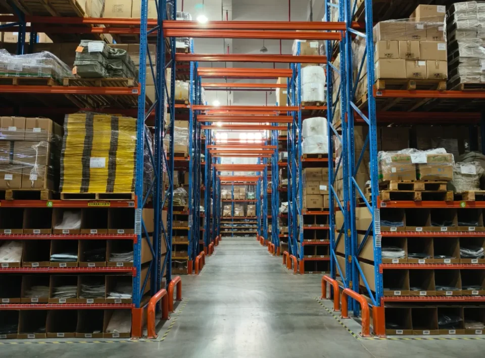 Cajas y mercancía envuelta distribuidas a lo largo de un pasillo de almacén.